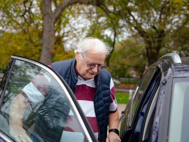 An older man getting into the back of a car